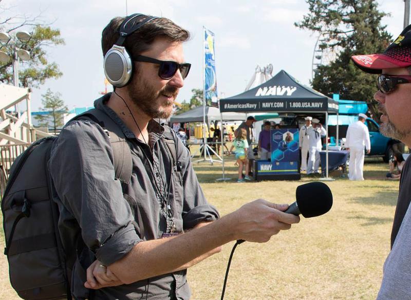 Reporter holding microphone and wearing headphones interviews man at fair