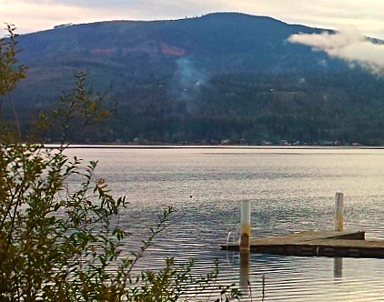 Old wooden dock extending into a large calm lake with a wooded mountain on the far side