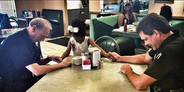 Young black child praying with two white police officers.