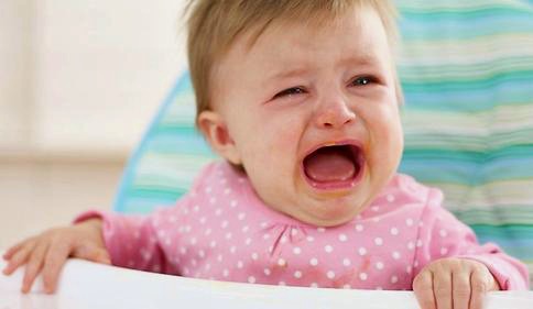 A crying one year old girl sitting in a high chair