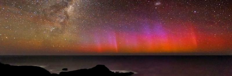 Stars in a dark sky, aurora australis on the ocean's distant horizon
