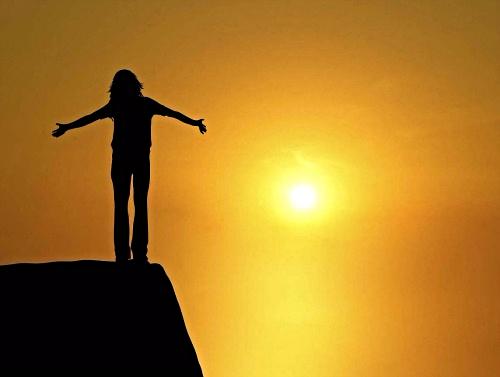 A woman standing on a cliff, rejoicing with the rising sun