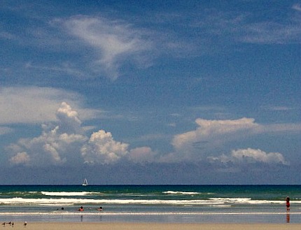 A quiet beach, gentle waves, and a blue sky with puffy, white clouds