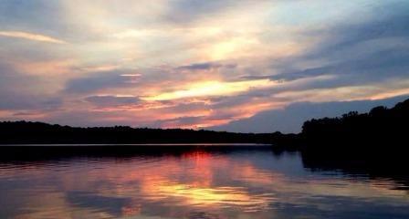 Sun peaking through clouds at sunset, over a calm lake