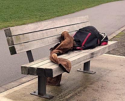 A homeless man's pack and few clothes, scattered on a lonely park bench 