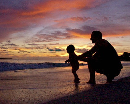 Father holding his baby daughter back from running into the water just before dawn