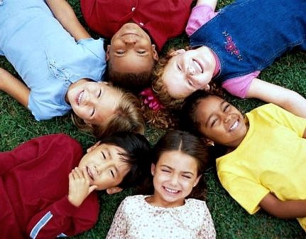Smiling children from around the world, lying in grass and looking up into the camera.