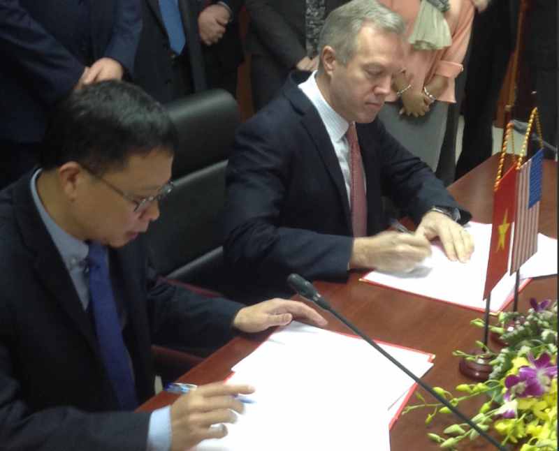 Two men sit at a table signing papers.