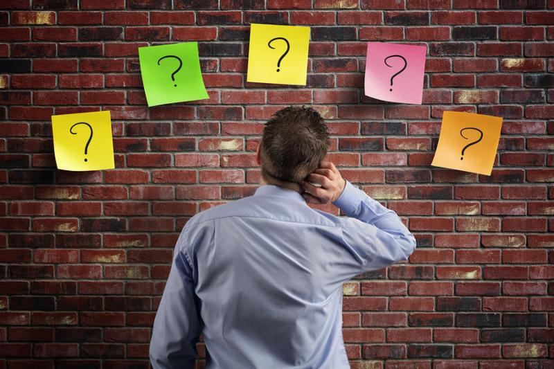 Choice and decisions  businessman thinking with question marks written on adhesive notes stuck to a brick wall