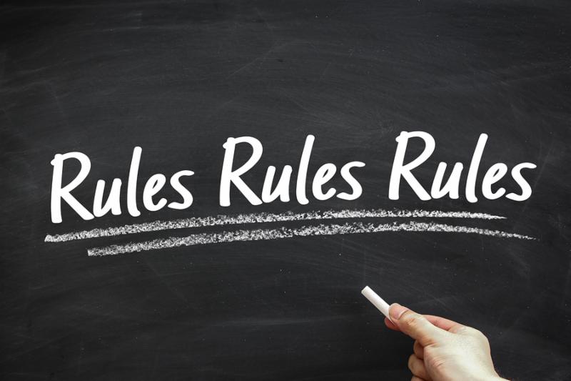 Text Rules written on the blackboard with hand holding white chalk aside.