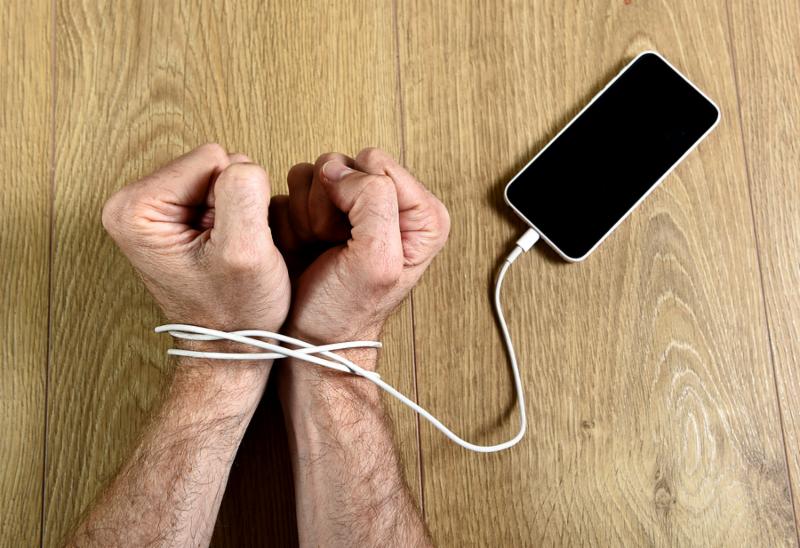 man hands trapped and wrapped on wrists with mobile phone cable as handcuffs in smart phone networking and communication technology addiction concept