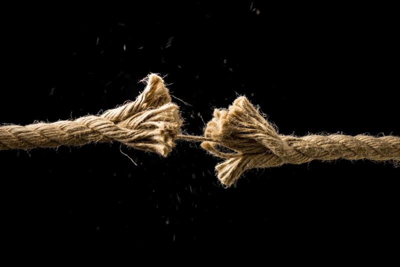 Concept of danger and risk with two ends of a frayed worn rope held together by the last strand on the point of snapping against a dark background with copyspace.