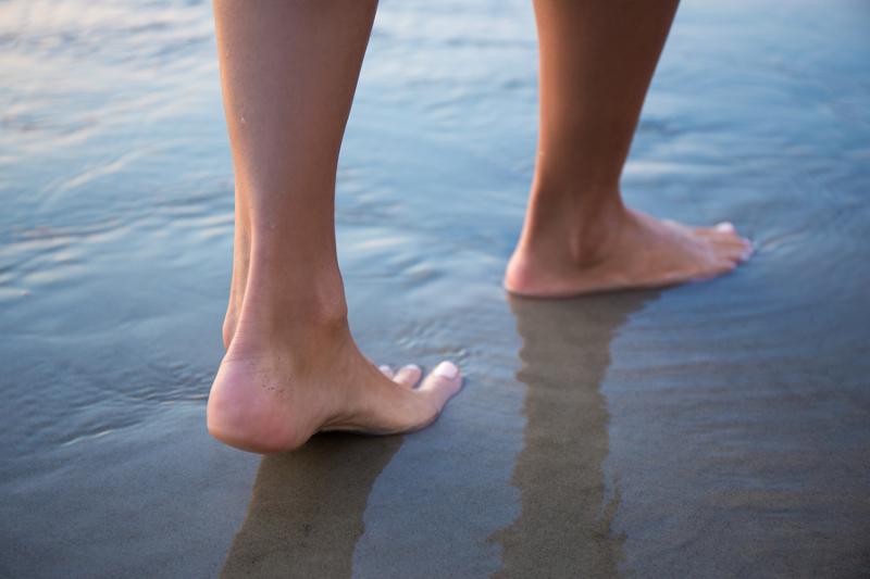 close up of female legs walking in water on beach