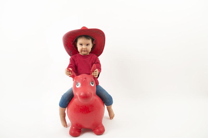 Little girl with red cowboy hat riding o toy horse isolated