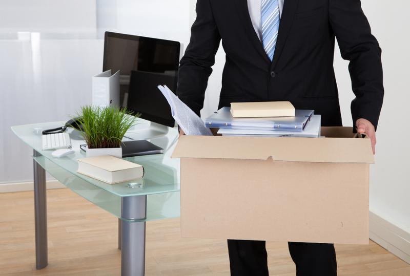 Businessman moving offices packing up all his personal belongings and files into a brown cardboard box