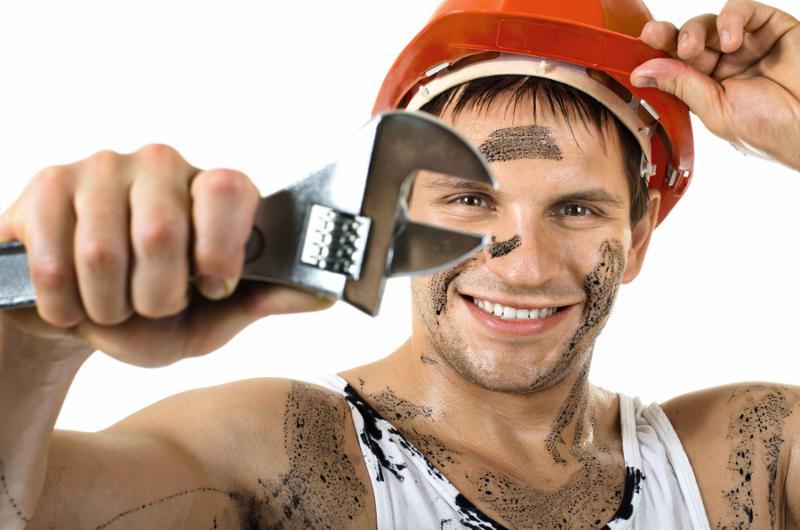 happy worker man dirty in safety helmet with big wrench in hands turn on and smile on white background isolated