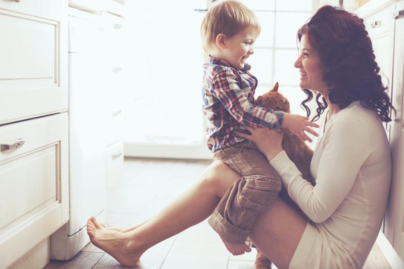Mother with her baby playing with pet on the floor at the kitchen at home