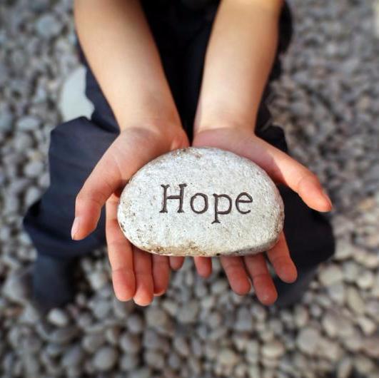 Child on a beach with hands cupped holding stone pebble with the word hope engraved concept for faith, love, spirituality and religion