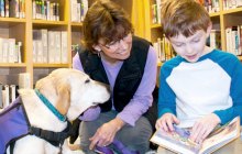 Child reading to dog and adult