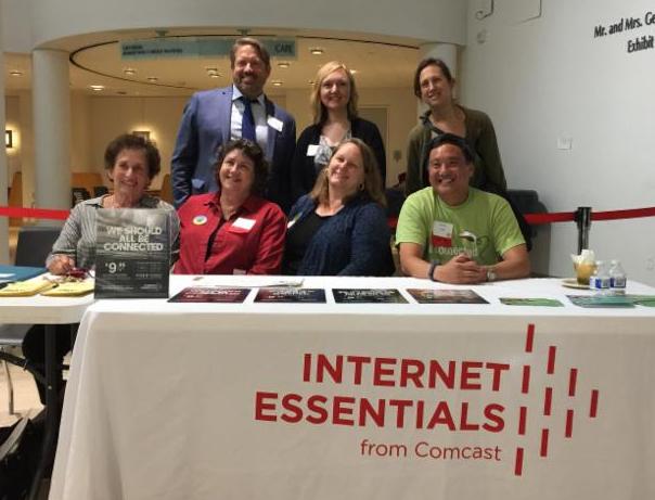 picture of people at a table with cloth that says Internet Essentials from Comcast.