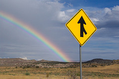 A merge sign with a rainbow in the background