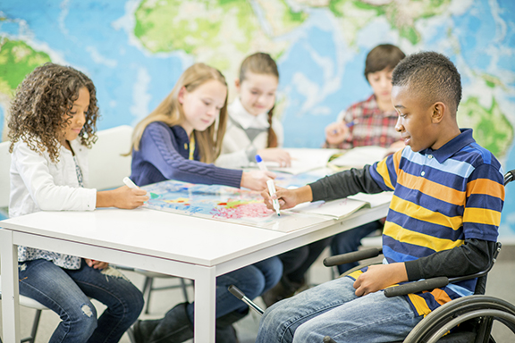 Child using a wheelchair working with other children on a map project.