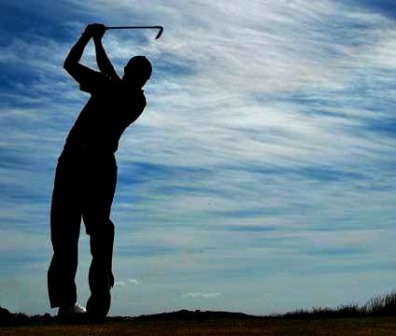 Sillhoette of a golfer swinging through his approach shot to the green