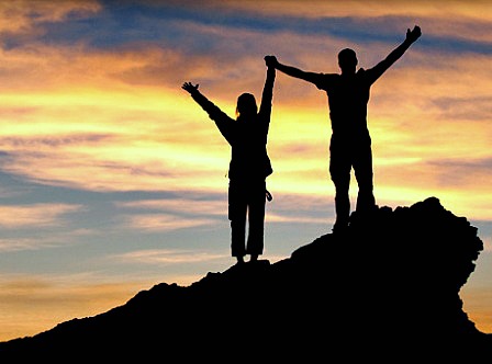 Two people standing on a summit against a brilliant sunset