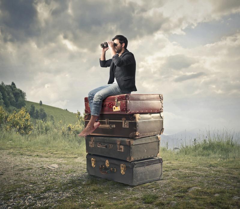 young man sitting on a pile of vintage suitcases looking with binoculars the panorama