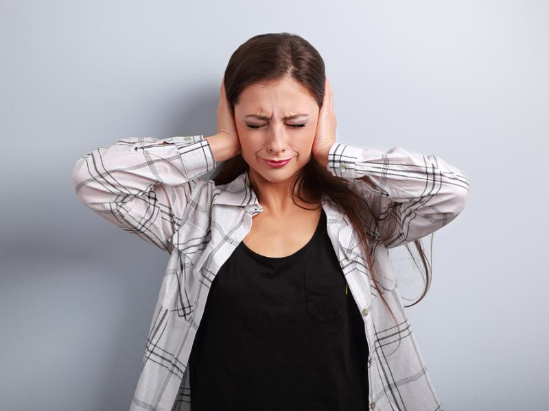 Stressed unhappy business woman closed ears the hands because not want the hear any sounds and noise on blue background